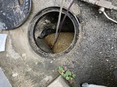 汚水が滞留した屋外排水桝を高圧洗浄している作業状況